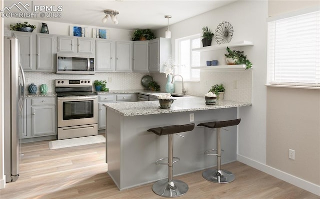 kitchen featuring a peninsula, appliances with stainless steel finishes, a sink, and decorative backsplash