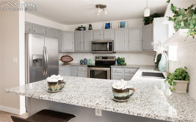 kitchen with light stone countertops, a peninsula, a sink, appliances with stainless steel finishes, and decorative backsplash