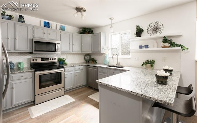 kitchen featuring appliances with stainless steel finishes, a peninsula, gray cabinets, light wood-style floors, and a sink