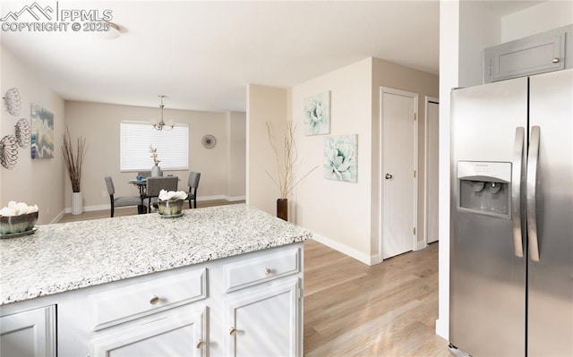 kitchen featuring light stone counters, baseboards, light wood-style flooring, and stainless steel fridge with ice dispenser