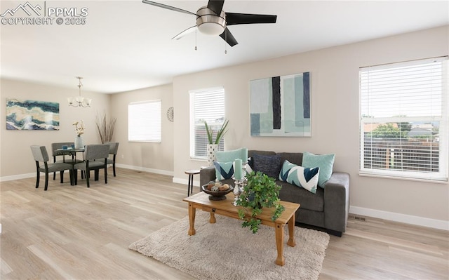 living room with light wood-style floors, baseboards, and ceiling fan with notable chandelier