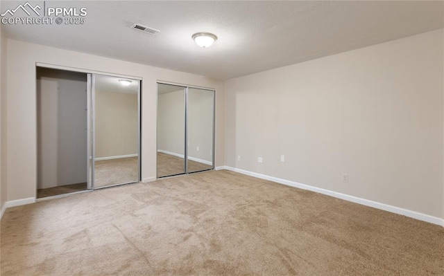 unfurnished bedroom featuring carpet floors, multiple closets, visible vents, a textured ceiling, and baseboards