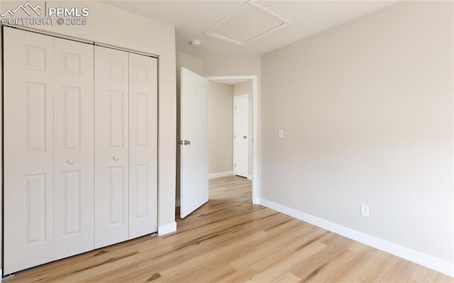 unfurnished bedroom with attic access, light wood-type flooring, a closet, and baseboards