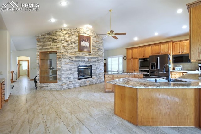 kitchen featuring arched walkways, a stone fireplace, light stone counters, a sink, and black appliances