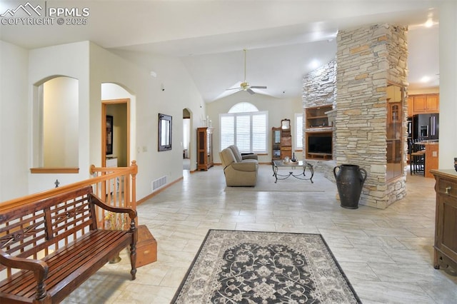 living area featuring baseboards, visible vents, a ceiling fan, a stone fireplace, and high vaulted ceiling