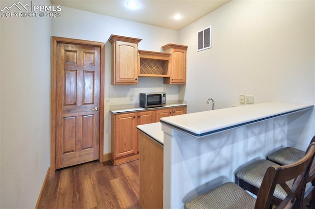 kitchen featuring visible vents, stainless steel microwave, dark wood-type flooring, a peninsula, and a kitchen breakfast bar