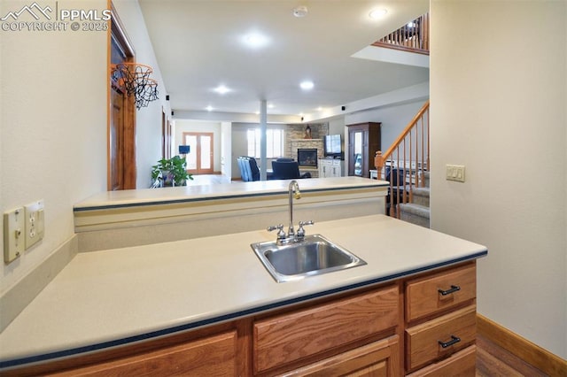 kitchen featuring brown cabinetry, light countertops, a fireplace, and a sink