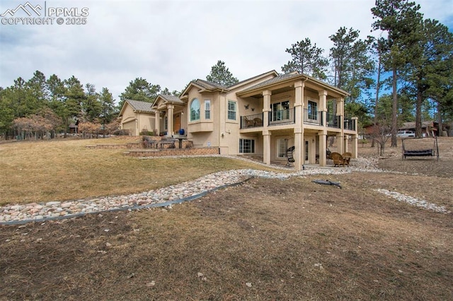 back of house featuring a lawn, a patio area, a balcony, and stucco siding