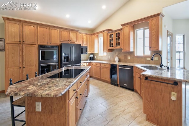 kitchen with lofted ceiling, a sink, black appliances, light stone countertops, and a kitchen breakfast bar