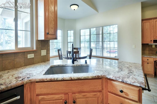 kitchen with decorative backsplash, dishwasher, light stone counters, a peninsula, and a sink