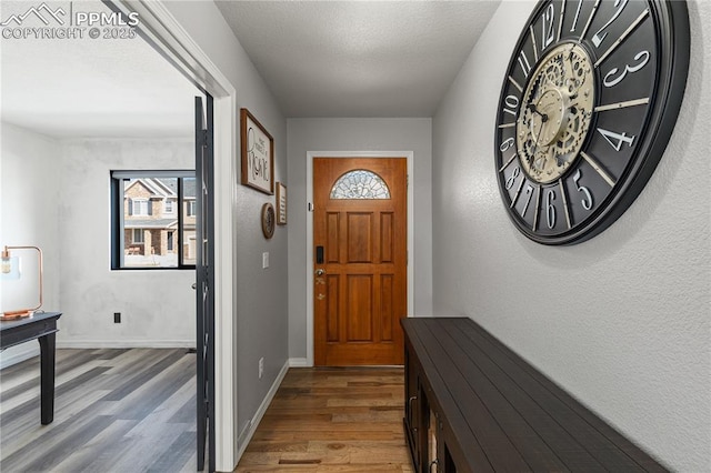 doorway to outside with a textured ceiling, baseboards, and wood finished floors