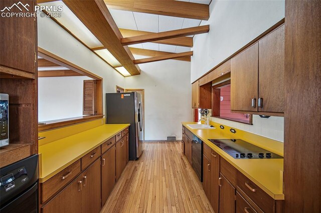 kitchen with light wood-style floors, black appliances, light countertops, a sink, and vaulted ceiling with beams