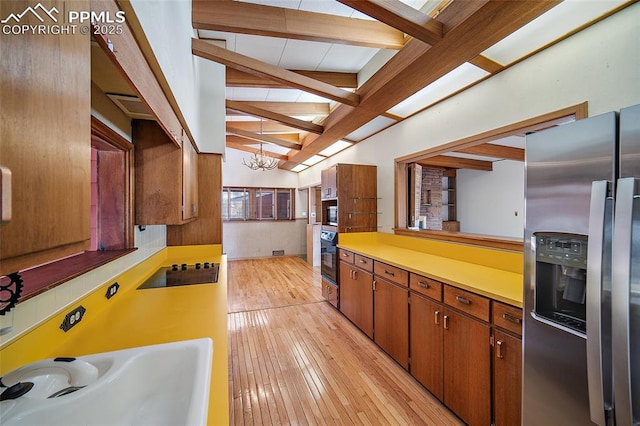 kitchen with light wood-type flooring, lofted ceiling with beams, light countertops, black appliances, and a sink