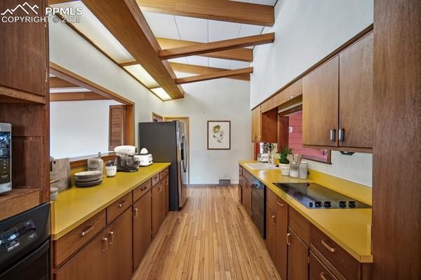 kitchen featuring beamed ceiling, light wood-type flooring, black appliances, a sink, and light countertops