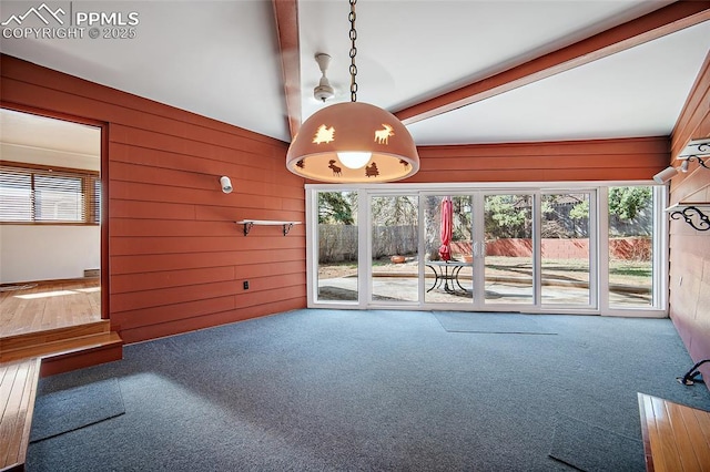 unfurnished dining area with wood walls, a wealth of natural light, and carpet floors