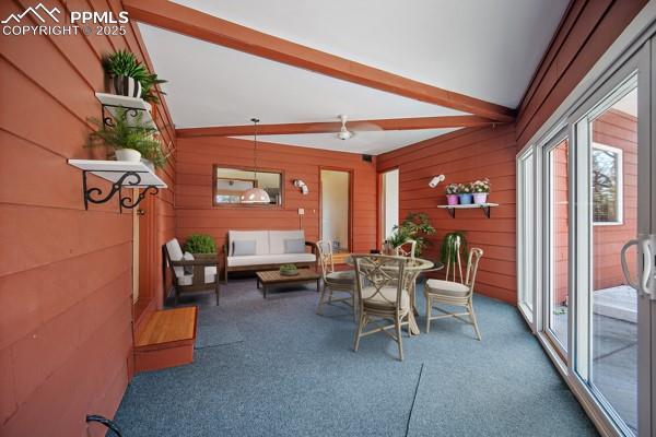 carpeted dining room with wood walls and vaulted ceiling with beams