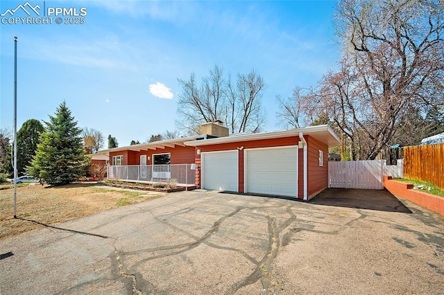 view of front of house featuring a chimney, an attached garage, fence, and aphalt driveway