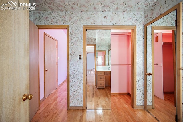 hallway featuring baseboards, light wood-style floors, and wallpapered walls