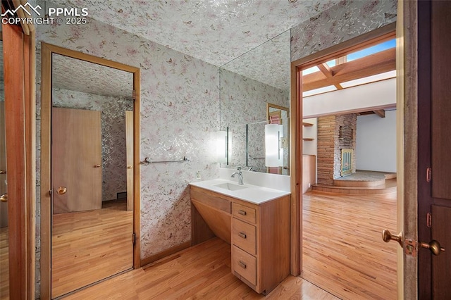 bathroom with vanity, a stone fireplace, wallpapered walls, and wood finished floors