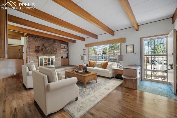 living room featuring beam ceiling, wood finished floors, and a fireplace