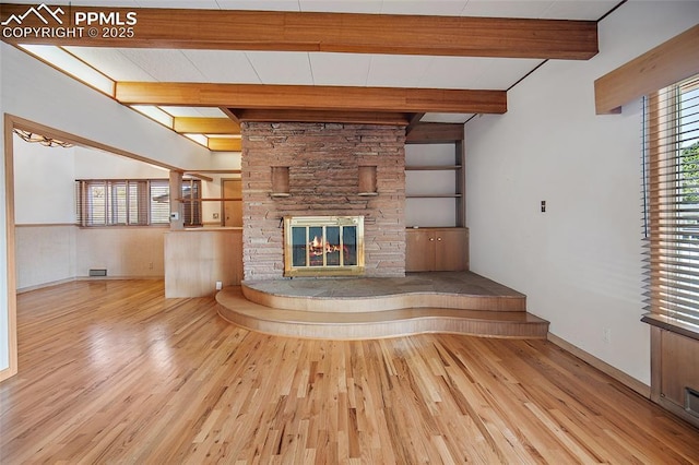 unfurnished living room with a fireplace, visible vents, beamed ceiling, and wood finished floors