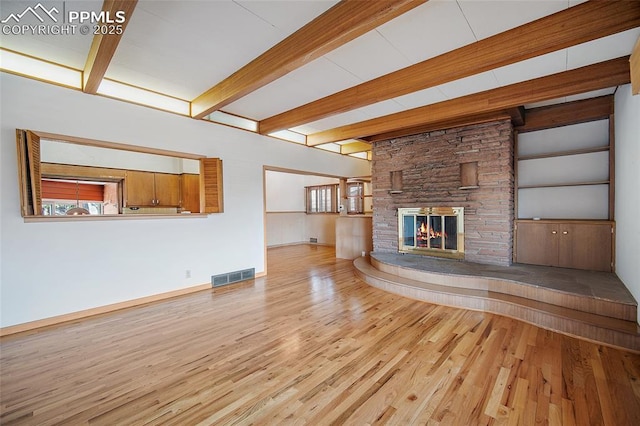 unfurnished living room featuring a healthy amount of sunlight, visible vents, beamed ceiling, and wood finished floors