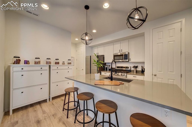 kitchen with light wood finished floors, stainless steel microwave, decorative backsplash, white cabinetry, and a sink