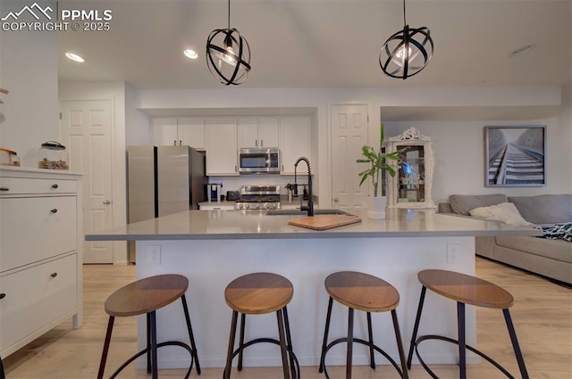 kitchen featuring tasteful backsplash, stainless steel appliances, light wood-style floors, white cabinetry, and a sink