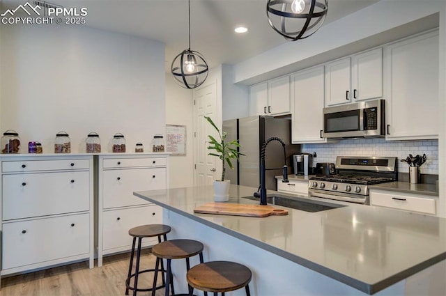 kitchen featuring white cabinets, a sink, stainless steel appliances, light wood-type flooring, and backsplash