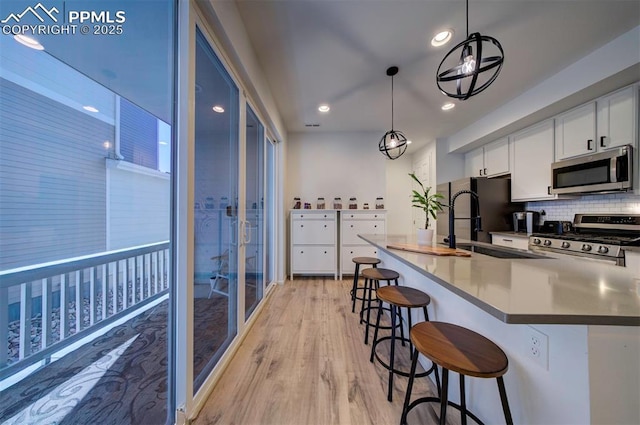 kitchen with light wood-style flooring, stainless steel appliances, white cabinets, tasteful backsplash, and a kitchen bar