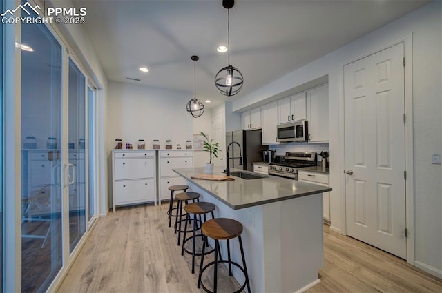 kitchen with a breakfast bar area, stainless steel appliances, a sink, light wood-type flooring, and decorative backsplash