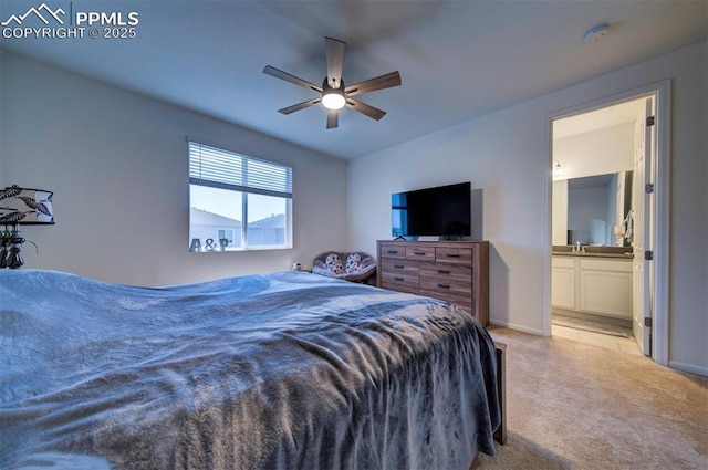 bedroom with baseboards, ensuite bathroom, a ceiling fan, and light colored carpet