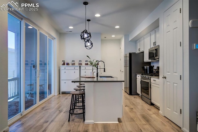 kitchen featuring light wood-type flooring, appliances with stainless steel finishes, dark countertops, and a kitchen bar