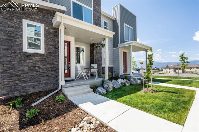 entrance to property with covered porch, stone siding, and a lawn