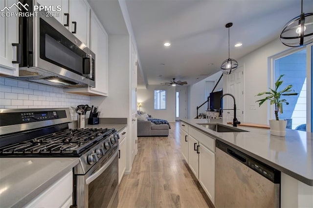 kitchen with a sink, white cabinets, open floor plan, appliances with stainless steel finishes, and backsplash