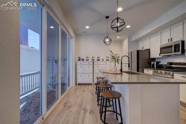 kitchen featuring a breakfast bar, stainless steel appliances, tasteful backsplash, light wood-style floors, and white cabinets