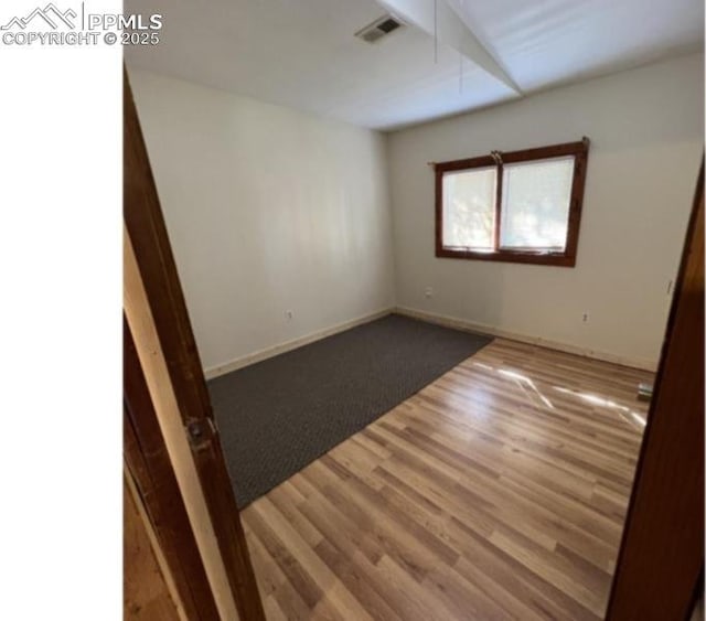 empty room featuring wood finished floors, visible vents, and baseboards