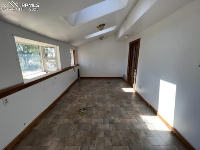 spare room featuring stone finish flooring, vaulted ceiling with skylight, and baseboards