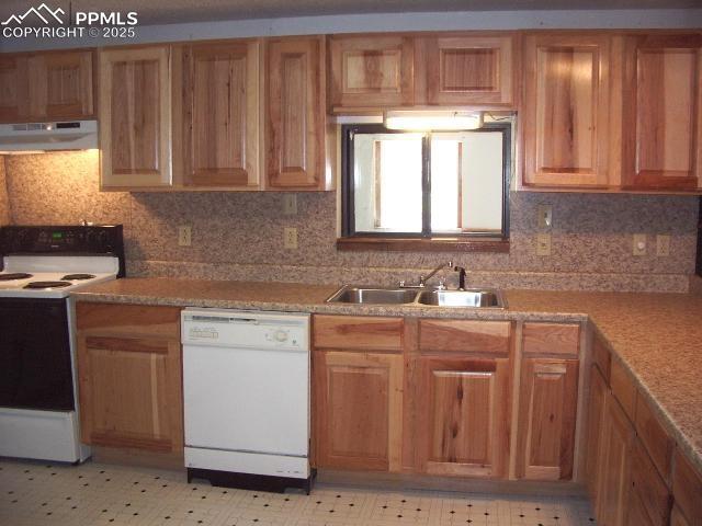 kitchen featuring white appliances, tasteful backsplash, light floors, under cabinet range hood, and a sink