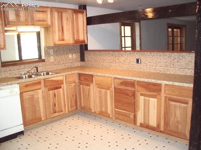 kitchen with light floors, white dishwasher, a sink, and light countertops