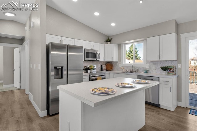 kitchen featuring stainless steel appliances, lofted ceiling, tasteful backsplash, light countertops, and white cabinetry