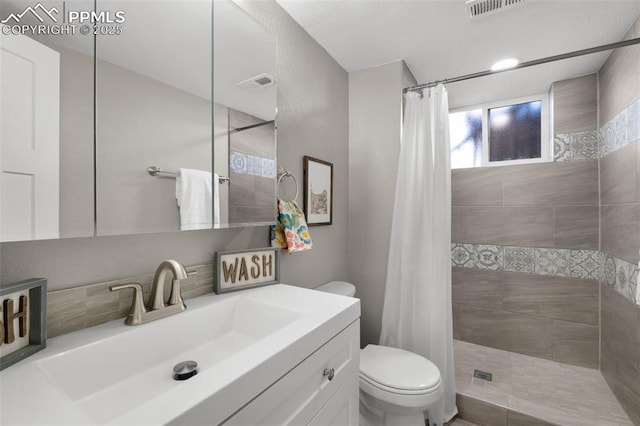 bathroom with visible vents, vanity, toilet, and tiled shower