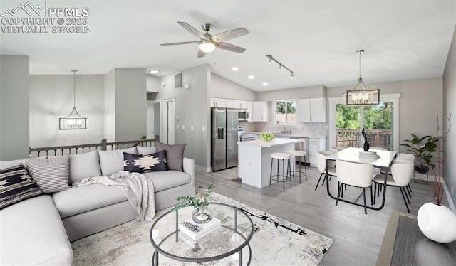 living area with light wood-style flooring, baseboards, vaulted ceiling, and ceiling fan with notable chandelier