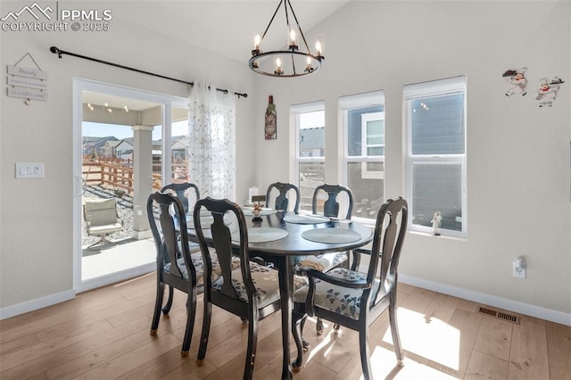 dining space featuring hardwood / wood-style floors, baseboards, visible vents, an inviting chandelier, and lofted ceiling