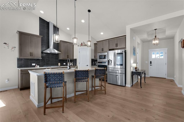 kitchen with wall chimney range hood, light countertops, light wood-style floors, appliances with stainless steel finishes, and a kitchen breakfast bar