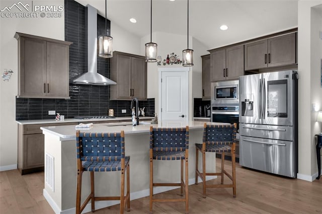 kitchen featuring light wood finished floors, wall chimney range hood, vaulted ceiling, decorative backsplash, and appliances with stainless steel finishes