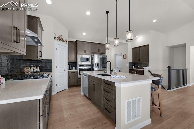 kitchen with visible vents, wall chimney range hood, dark brown cabinetry, appliances with stainless steel finishes, and a sink