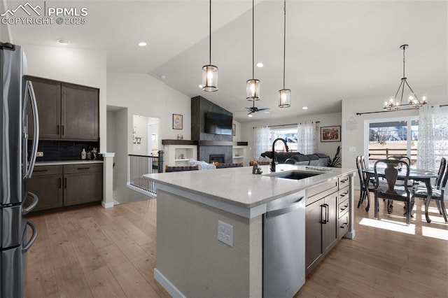 kitchen featuring light wood finished floors, lofted ceiling, appliances with stainless steel finishes, a fireplace, and a sink