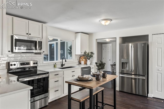 kitchen featuring tasteful backsplash, appliances with stainless steel finishes, dark wood-type flooring, light countertops, and a sink