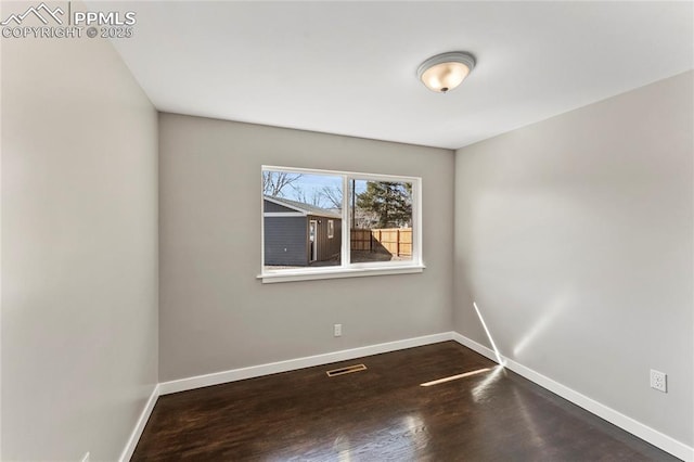 spare room featuring wood finished floors, visible vents, and baseboards